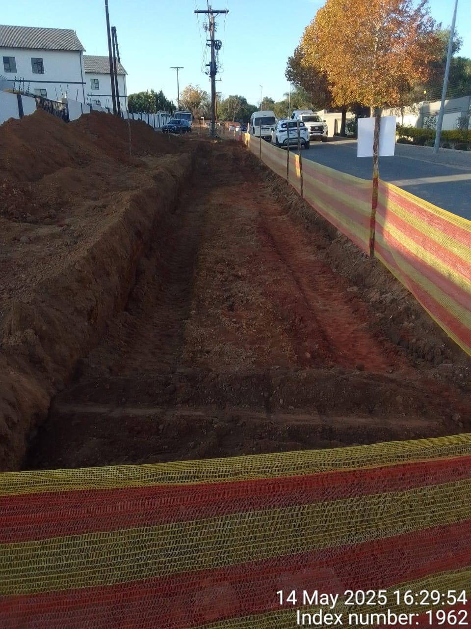 Open service trench with safety barrier netting alongside the road